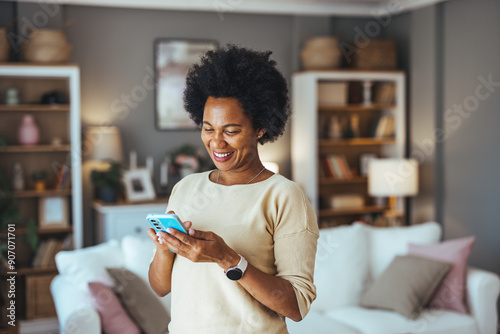 Young woman using the mobile phone at home. Portrait of a happy and connected woman at home, who uses her smartphone to stay in touch with her loved ones, navigate the digital world