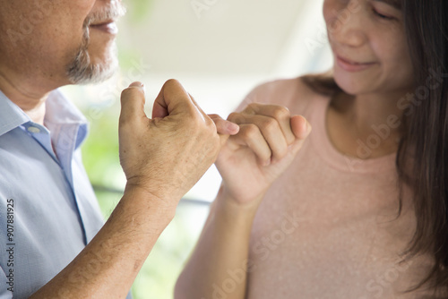 Senior man hooking little finger for pinky promise with middle aged daughter, concept image for family reunion, family togetherness, lovely family promise