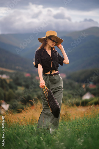 Fashionable confident woman wearing trendy summer hat, sunglasses, linen shirt, green maxi skirt, silver cowboy boots, holding black wicker straw bag, walking outdoor. Full-length fashion portrait 