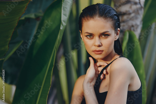 Attractive young woman with hand on chin posing in front of tropical palm trees against clear sky background