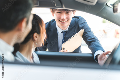 自動車購入・査定・買取にきた顧客を接客するセールスマンの若いアジア人男性 