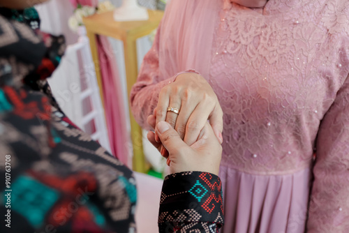 A pair of hands holding each other, wearing engagement rings and kebaya dresses. Boyfriend proposing to his girlfriend to get married. Concept of people relationship, ring present and love