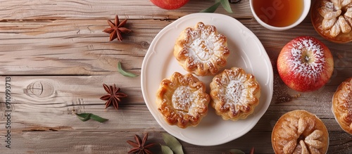 Apple tarts arranged on a white plate with a cup of tea set against a wooden backdrop with space for additional image