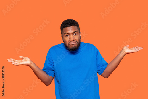 Man Wearing Blue Shirt Shrugging Shoulders Against Vibrant Orange Background Displaying Confusion or Indecision During Late Afternoon