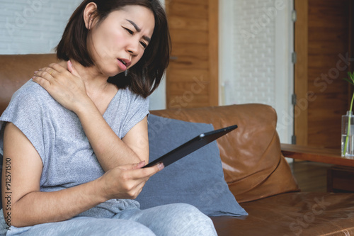 Asian woman suffering from neck pain and muscle strain in shoulders after using and holding tablet too long