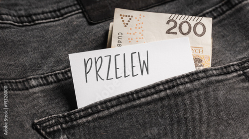 White card with a handwritten inscription "Przelew", inserted into the pocket of gray pants jeasnow, next to Polish banknotes PLN (selective focus), translation: Transfer