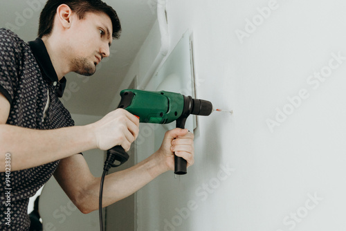 A young man drills a hole in the wall.