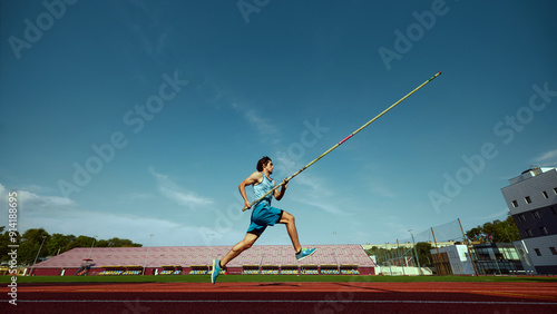 High jump training in progress, with a strong and focused pole vaulter in motion, running wit pole at outdoor stadium. Concept of sport, competition, tournament, active lifestyle, strength. Banner