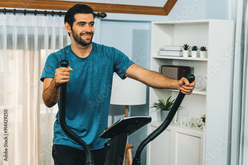 Athletic and sporty man running on elliptical running machine during home body workout exercise session for fit physique and healthy sport lifestyle at home. Gaiety home exercise workout training.