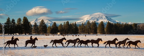 A metal scurpture of two cowboys and a string of horses with the three sisters mountains in background.