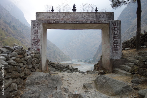 Weathered welcome sign marks the entrance to manang district in nepal, with a river and mountains visible through the gate