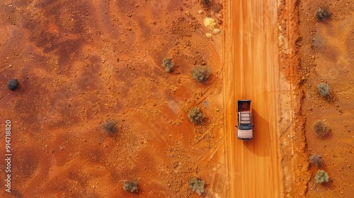 A lone truck travels down a long, dirt road in a dry, red desert landscape.