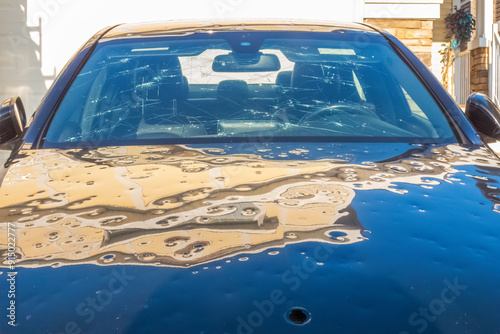 Significant hail damage to a parked vehicle. The windshield is extensively cracked, and the hood is dented with multiple impact points.