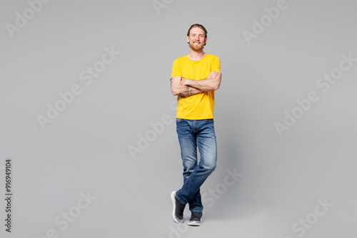 Full body smiling happy cheerful satisfied young man he wear yellow t-shirt casual clothes hold hands crossed folded look camera isolated on plain grey background studio portrait. Lifestyle concept.