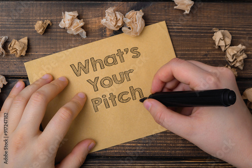 A hand is writing on a piece of paper that says What's your pitch.