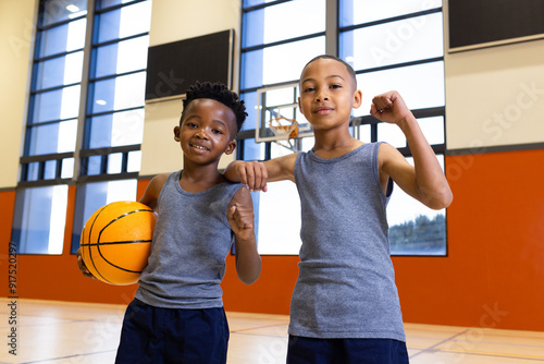 In school gym, boys holding basketball and flexing muscles, smiling confidently