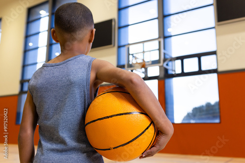 Holding basketball, boy standing in school gymnasium, preparing for practice