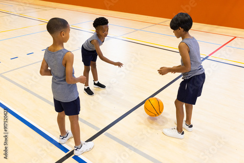 Playing basketball in school gym, three boys practicing dribbling and passing