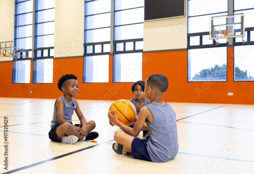 In school gym, kids sitting on floor with basketball, enjoying conversation