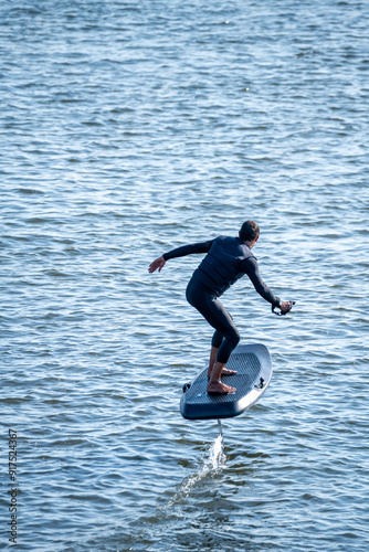 Surfer balances on electric hydrofoil board, gliding above rippling water with arms outstretched