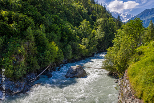 view of the river dora baltea with forest in the aosta valley with the mont blanc massif in the background and blue sunny cloudy sky 