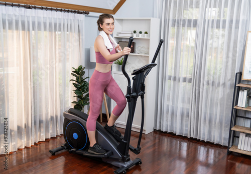 Athletic and sporty woman running on elliptical running machine during home body workout exercise session for fit physique and healthy sport lifestyle at home. Gaiety home exercise workout training.