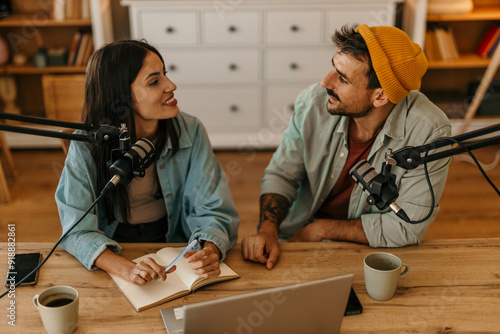 Beautiful woman and man smiling as they chat into microphones during a podcast session