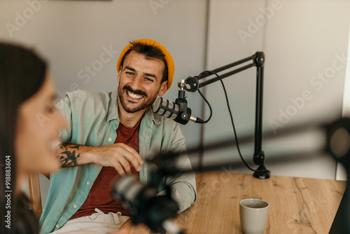 Two cheerful radio hosts in headphones recording podcast in broadcasting. Focus on a male guest talking