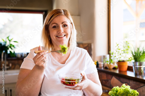 Portrait of beautiful young overweight woman choosing healthy food, eating vegetable salad.