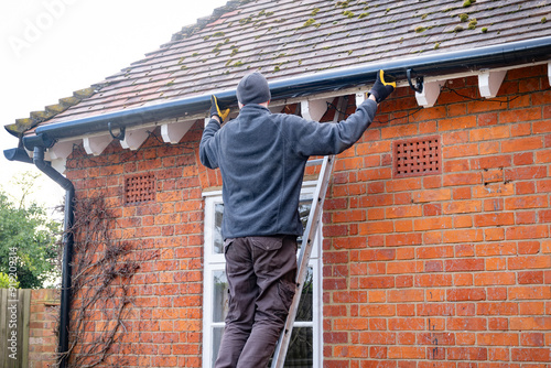 Man on a ladder fixing rain gutter on a UK house