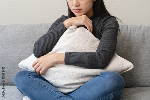 Unhappy anxiety young Asian woman covering her face with pillow on the cough in the living room at home.