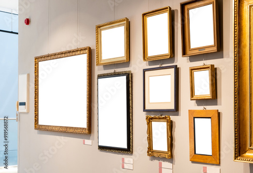 Lots of empty blank cut out white gold painting frames hanging on a wall inside a modern museum or art gallery generic interior, many paintings on one wall wooden panels, top lighting nobody no people