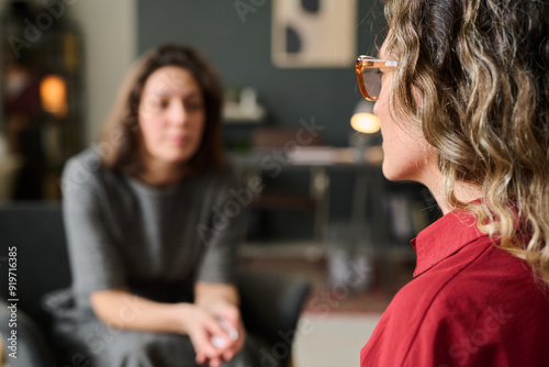 Two women engaging in a one-on-one counseling session in a cozy, well-lit room, one expressing herself while the other listens attentively. Background elements include furniture and decor