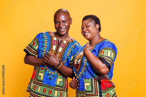 Smiling cheerful couple in love standing and looking at camera with joyful expression. Carefree black man and woman spouse posing together for studio portrait on orange background