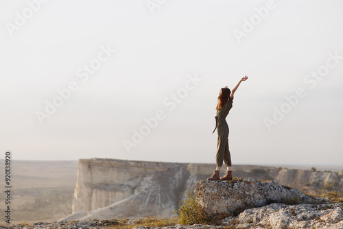 Woman triumphantly raising arms on mountain summit during adventurous travel hike in nature landscape