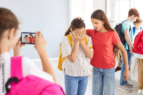 School bullying scene with teenage kids fighting in hallway with their classmate, taking video on smartphone camera. Stressed female victim student bullied by group of girls classmates in college.