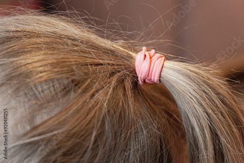 Close-up of a ponytail of hair with a pink elastic band. The girl's hairstyle, brittle dry hair.