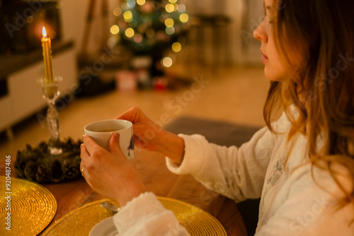 Mujer en el salón de casa decorado para las Navidades con una taza de té caliente en las manos. Momento de calma y relajación. 