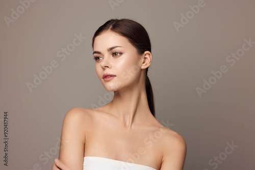 Photo of beautiful young woman in a white dress posing with hands on her hips and looking at the camera, isolated on a gray background