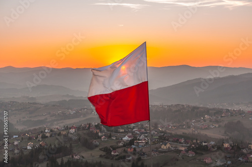 Biało-czerwona flaga Polski na tle zachodzącego słońca w górach - Ochodzita, Koniaków