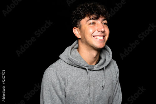 Portrait of young Caucasian man with curly hair about 25 years old, smiling while posing on black background