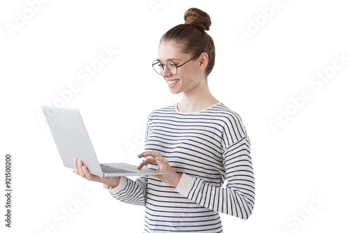 Indoor photo of positive teenage girl standing with laptop, smiling at great content from social networks, pressing fingers to touchpad in order to browse web pages