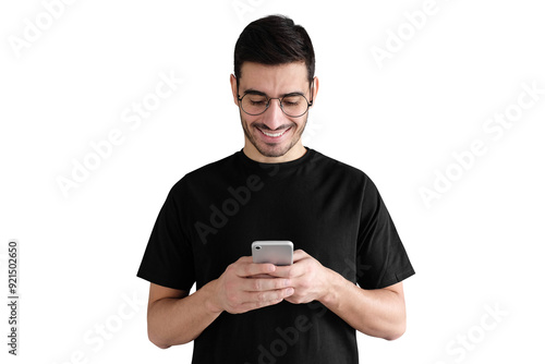 Young man standing against, looking at screen of phone, browsing web and smiling nicely while chatting