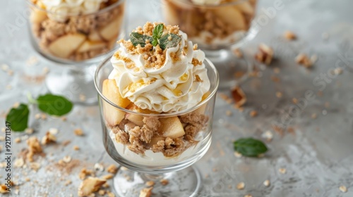 Dessert, portioned apple trifle with oat crumble, spiced cake, custard and whipped cream in a glass goblet on a light concrete background. Apple desserts, portioned desserts in glasses