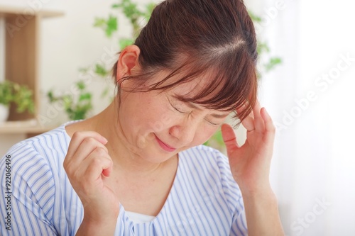 頭が痛くてこめかみを押さえるシニア女性