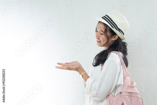 Portrait of Asian woman wearing straw hat and pink bag looking aside as if showing product in her hand, product advertising mockup copy space