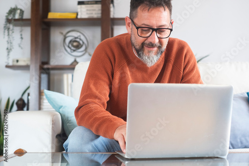 Modern man working as a freelance professional from home, using a laptop while sitting on a comfortable couch, balancing digital tasks with social media browsing, representing remote work business