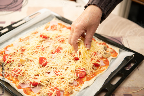 close up of elderly female hands putting grated cheese on an home made pizza. Home made pizza with mushrooms, tomato and cheese. Tasty Italian food.