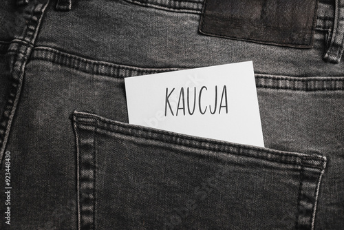 White card with a handwritten inscription "Kaucja", inserted into the pocket of gray pants jeasnow (selective focus), translation: Bail