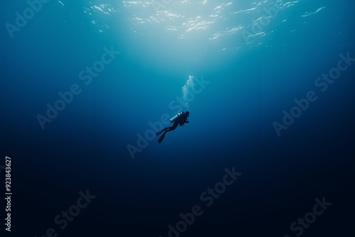 A lone scuba diver swims beneath the surface of a tranquil, deep blue ocean, creating a sense of adventure and serenity.